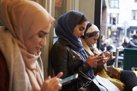 Group Of British Muslim Women Texting Outside Coffee Shopの写真素材