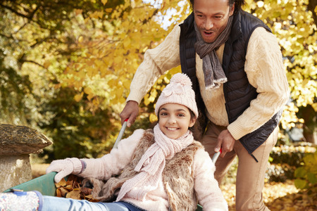 Father In Autumn Garden Gives Daughter Ride In Wheelbarrowの写真素材