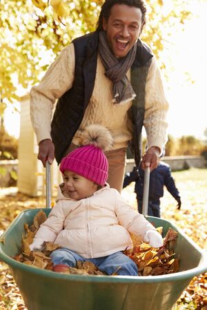 Father In Autumn Garden Gives Daughter Ride In Wheelbarrowの写真素材