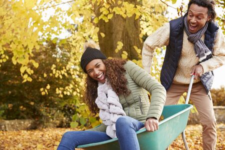 Man In Autumn Garden Gives Woman Ride In Wheelbarrowの写真素材