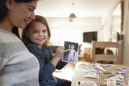 Mother And Daughter Sitting At Table Looking Photos