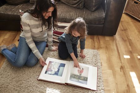 Mother And Daughter At Home Looking Through Photo Albumの写真素材