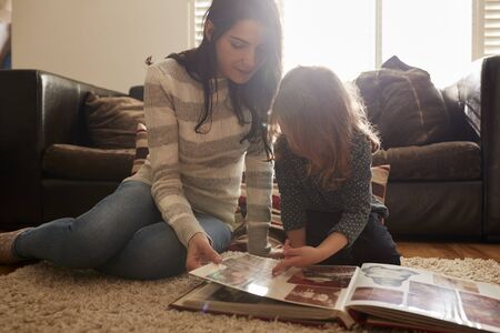Mother And Daughter At Home Looking Through Photo Albumの写真素材