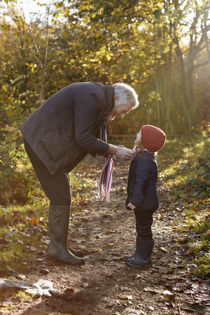 Grandfather Tying Granddaughter's Scarf On Autumn Walkの写真素材