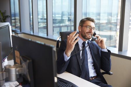 Businessman Making Phone Call Sitting At Desk In Office