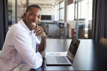 Young black man in office with laptop smiling to camera