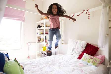 Young Girl Having Fun Jumping On Bed In Bedroomの写真素材