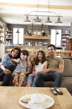 Family Sitting On Sofa In Open Plan Lounge Watching Televisionの写真素材