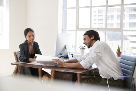 Young man and woman looking at documents across office desksの写真素材