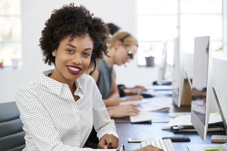Young black woman with headset smiling to camera in officeの写真素材