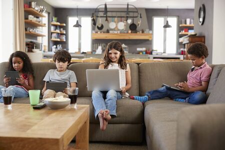 Group Of Children Sitting On Sofa Using Digital Devicesの写真素材