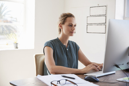 Young white woman working in office using computer, close upの写真素材