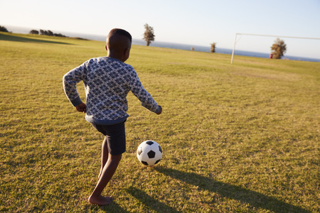 Elementary school boy playing football in an open fieldの写真素材