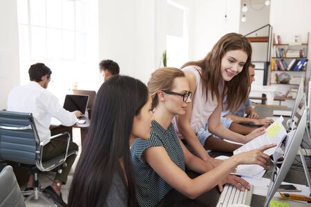 Three women working together at computer in open plan officeの写真素材