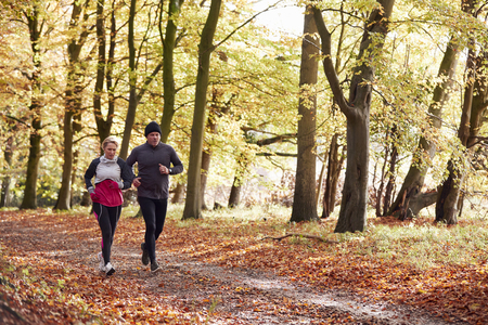 Mature Couple Running Through Autumn Woodland Togetherの写真素材