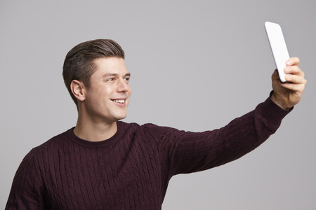 A smiling young man taking a selfie with his smartphoneの写真素材