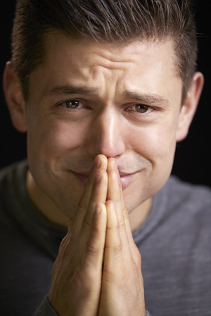 Close up of a worried young man with hands clasped, verticalの写真素材