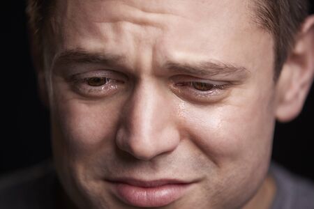 Close up portrait of crying young white man looking downの写真素材