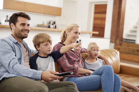 Family Sitting On Sofa In Open Plan Lounge Watching Televisionの写真素材