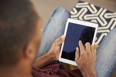 Man Sitting On Sofa At Home Looking At Digital Tablet