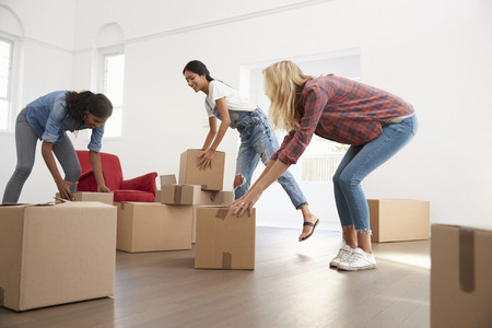 Three Female Friends Carrying Boxes Into New Home On Moving Dayの写真素材