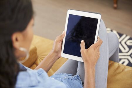 Woman Sitting On Sofa At Home Looking At Digital Tabletの写真素材