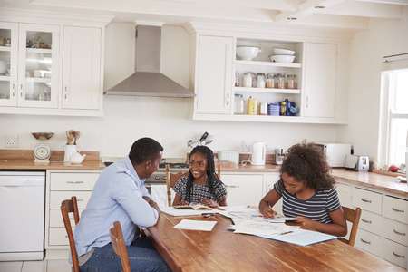 Father Helping Two Daughters Sitting At Table Doing Homeworkの写真素材