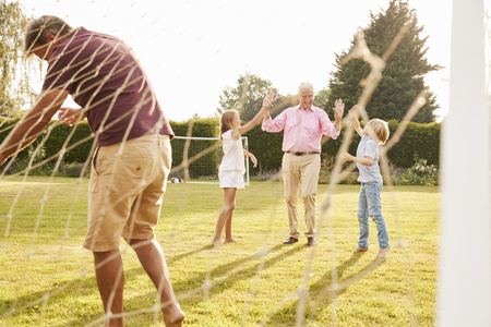 Granddad, dad and pre-teen kids playing footballの写真素材
