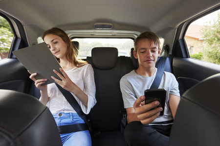Teenage Children Using Digital Devices On Family Road Tripの写真素材