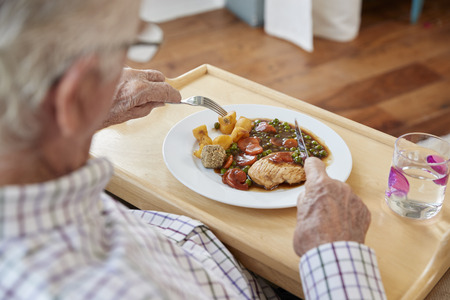 Over shoulder view of senior man eating dinner at homeの写真素材