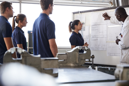 Engineer instructing four apprentices at white boardの写真素材