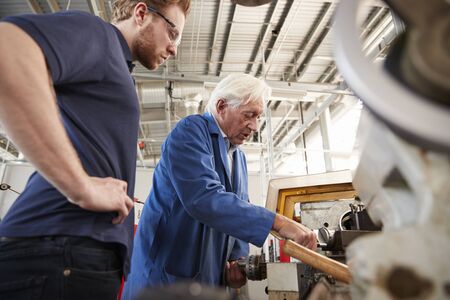Senior engineer demonstrating equipment to apprentice at machine bench, low angleの写真素材