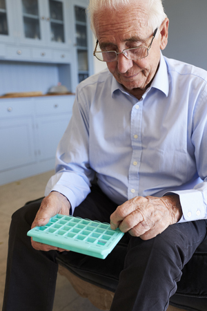 Senior Man At Home Using Pill Organiser For Medicationの写真素材
