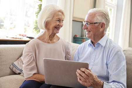 Senior Couple Sitting On Sofa Using Laptop At Home Togetherの写真素材
