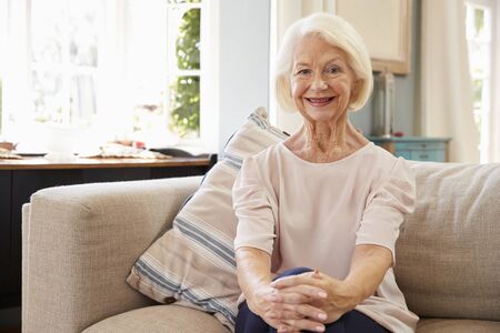 Portrait Of Smiling Senior Woman Sitting On Sofa At Home