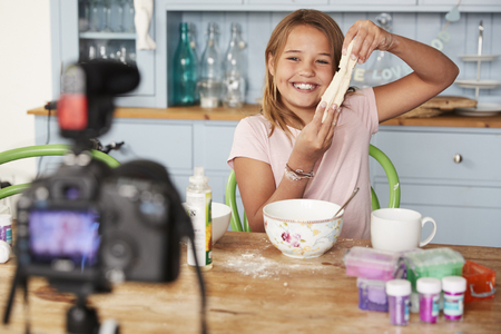 Young girl video blogging in a kitchen showing dough mixtureの写真素材