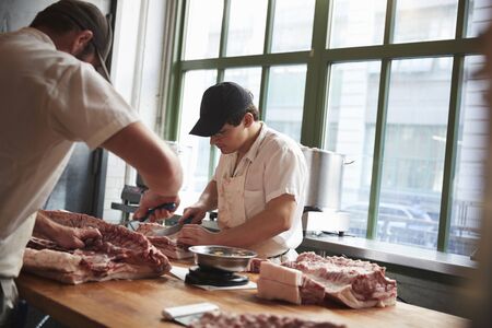 Two butchers cutting meat to sell at a butcher's shopの写真素材