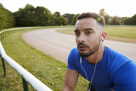 Male athlete wearing earphones at running track, close upの写真素材