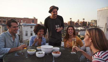 Six adult friends laughing at a table on a rooftop, close upの写真素材