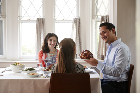 Jewish man holding challah bread at Shabbat meal with familyの写真素材