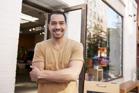 Young Hispanic shop owner smiling to camera outside his shopの写真素材