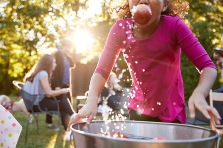 Pre-teen girl apple bobbing, with apple in mouth, close up