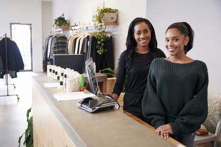 Two women smiling behind the counter in clothing storeの写真素材