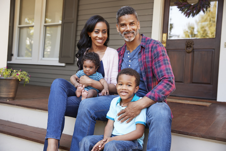 Family With Baby Son Sit On Steps Leading Up To Porch Of Homeの写真素材