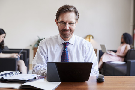 Businessman using laptop at desk, colleagues in background