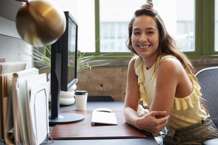 White woman at a computer in an office smiling to cameraの写真素材