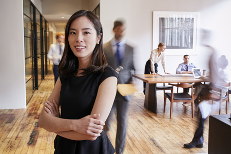 Portrait of young Asian woman in a busy modern workplaceの写真素材
