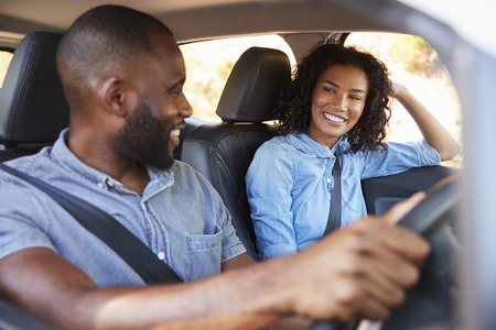 Young black couple in car on road trip smiling at each other