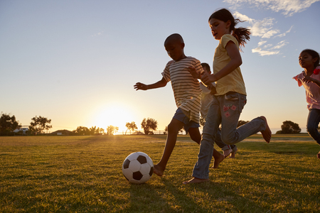 Four children racing after a football plying on a fieldの写真素材