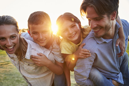 Young couple piggybacking their young children outdoors